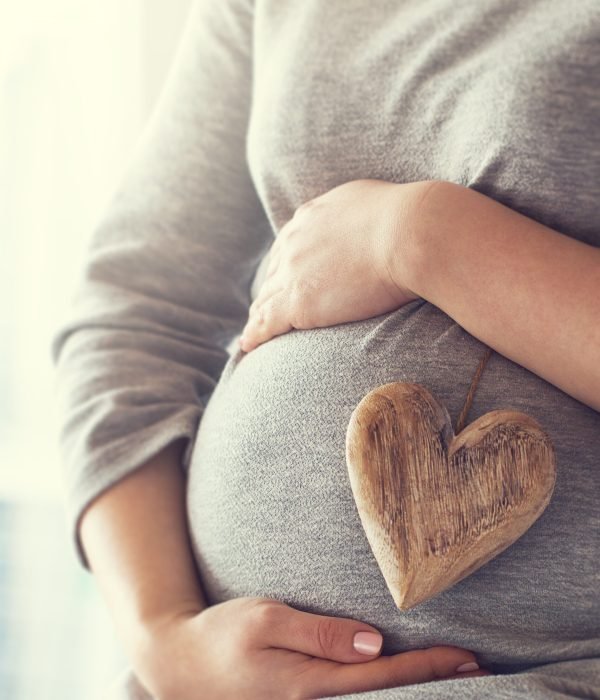 Young pregnant woman holds wooden heart. Love concept. Pastel toning